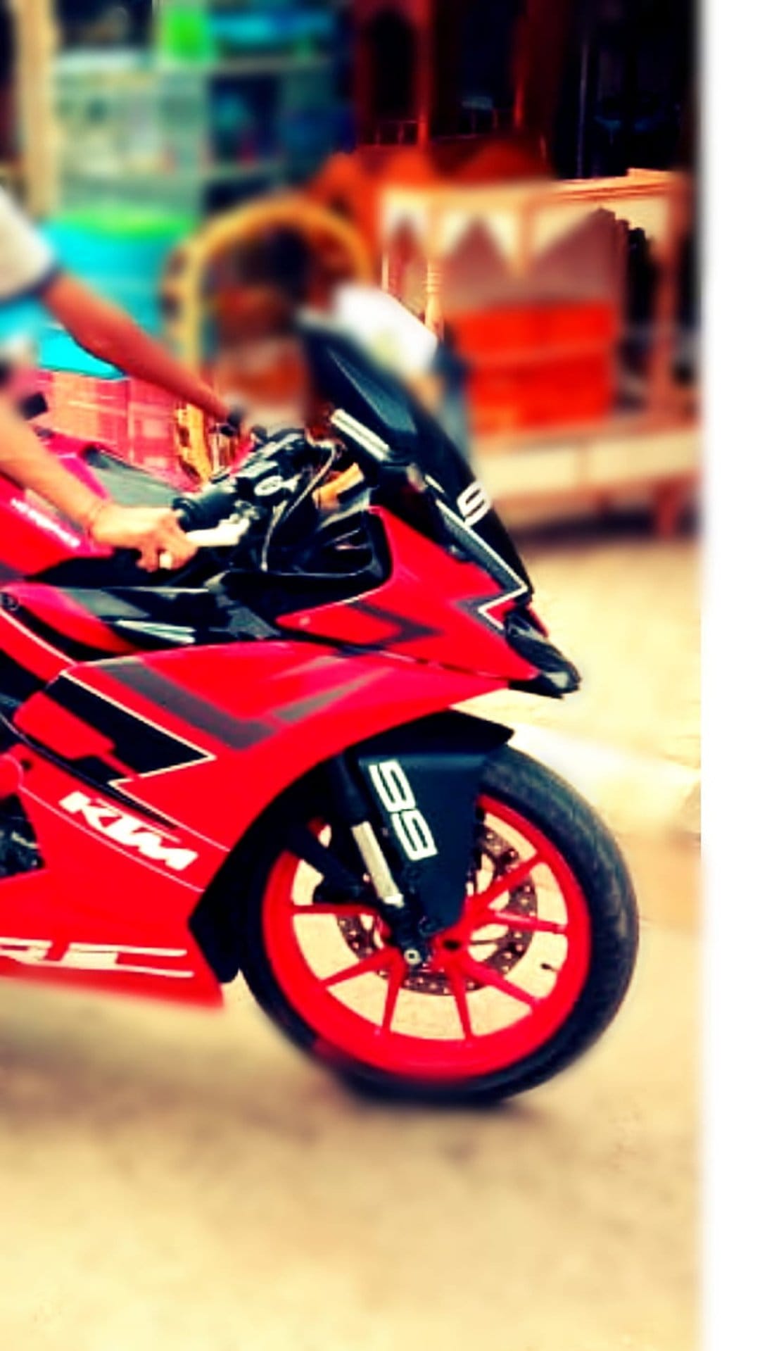 Red KTM RC motorcycle with a rider's hand on the handlebar against a colorful blurred street background.