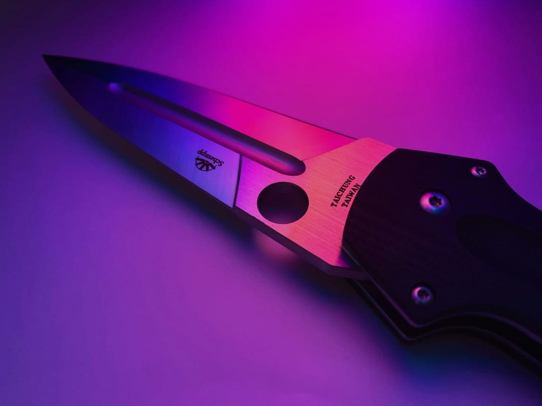 Spyderco knife blade with purple lighting, Taichung engraving, and a textured handle in a macro close-up.