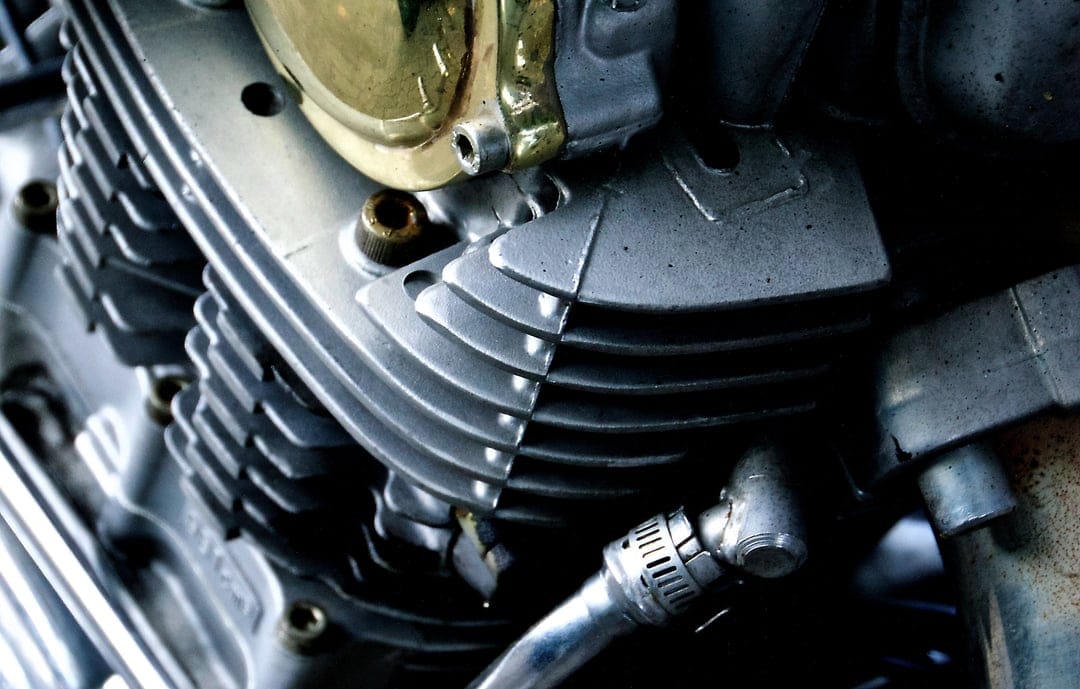 Motorcycle engine cylinder head cooling fins with metallic textures, silver bolts, and industrial dark shadows.