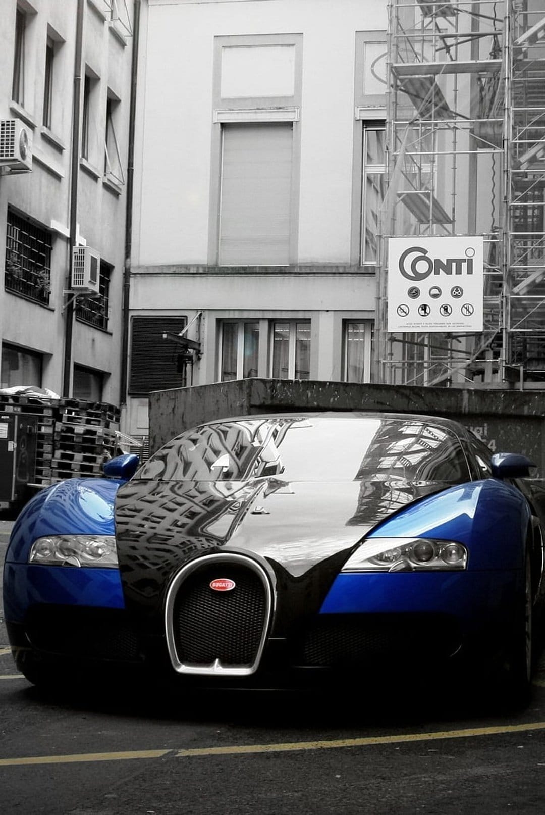Bugatti Veyron hypercar parked in a narrow alley with metallic scaffolding reflecting off the blue hood.
