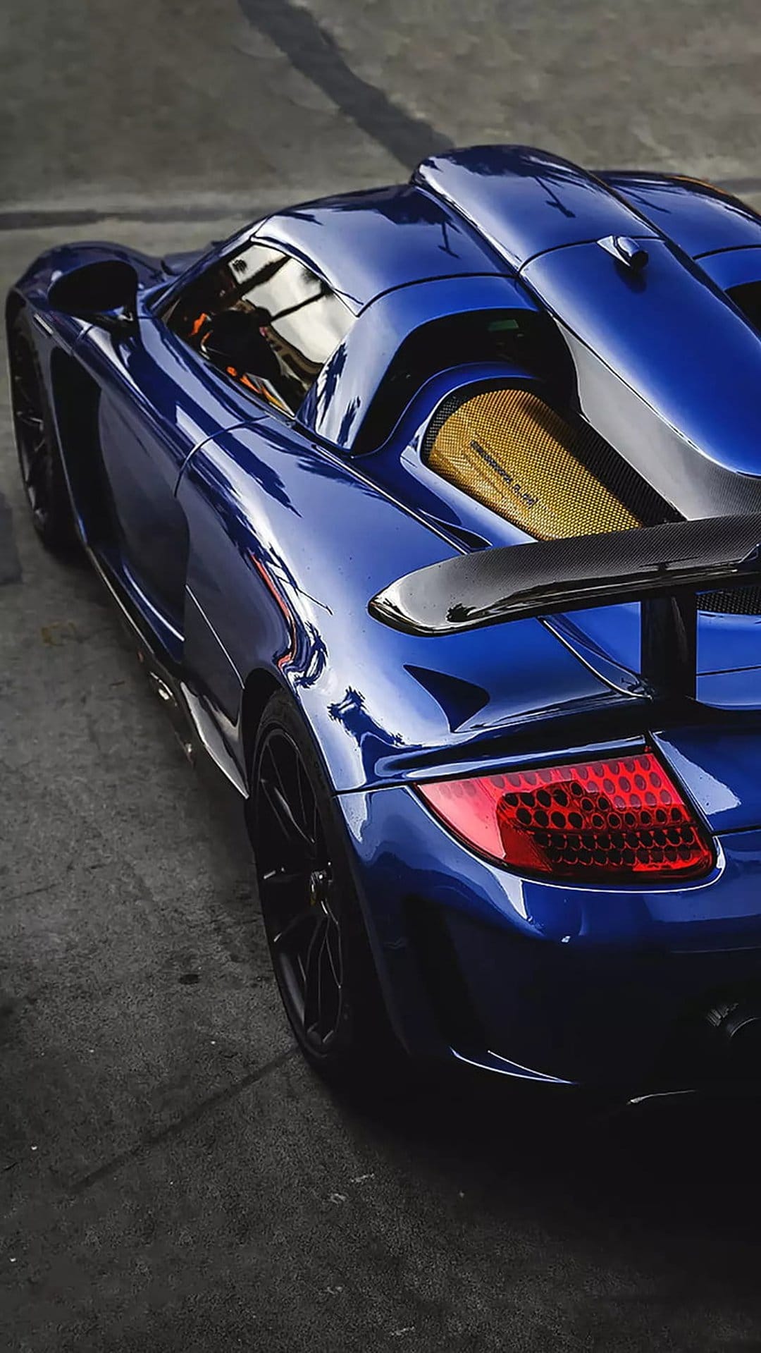 Porsche Carrera GT in blue paint with a black rear wing, red taillights, and a gold textured engine cover.