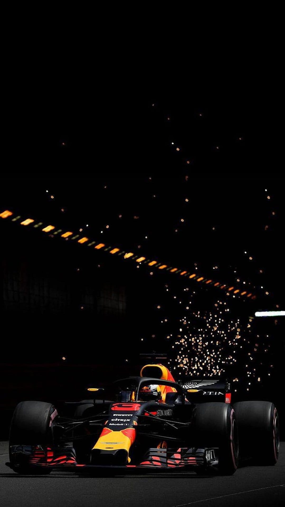 Formula 1 car releases bright orange sparks from its chassis on a dark night track under stadium lights.