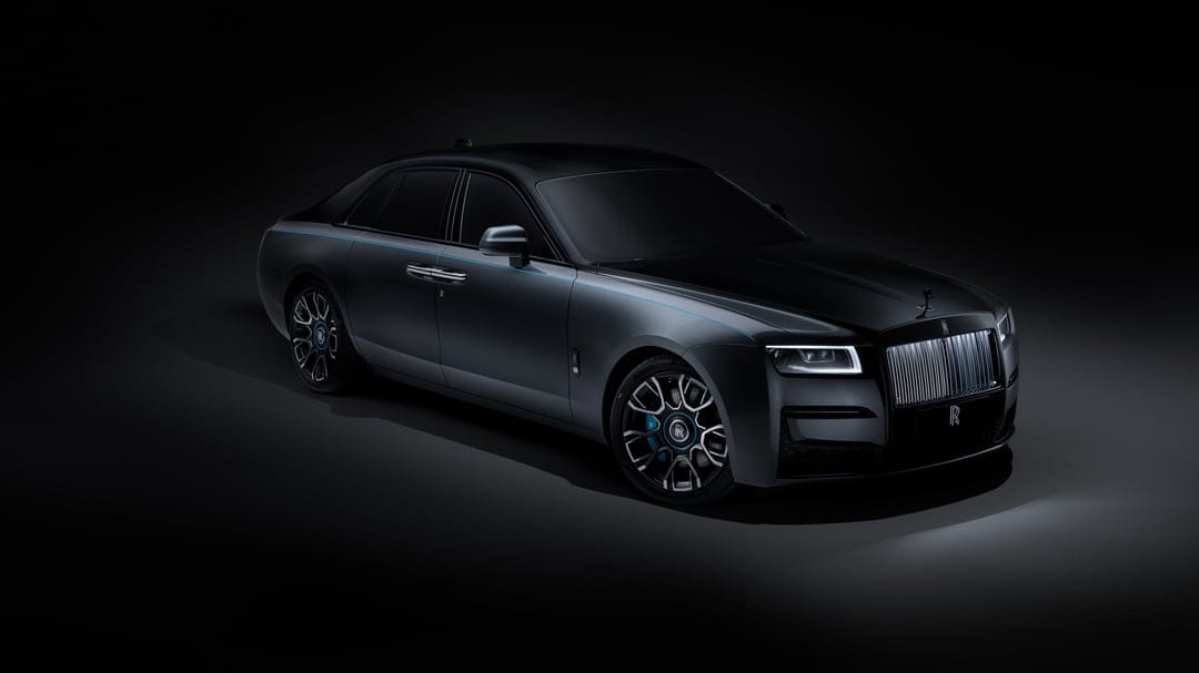 Side profile of a matte black luxury sedan with a blue coachline and illuminated grille in a dark studio.
