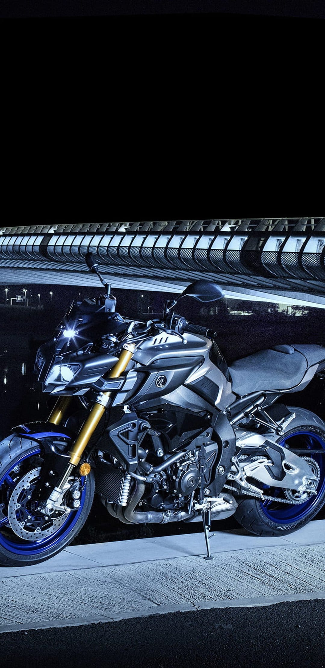 Yamaha MT-09 motorcycle parked on asphalt under a glowing bridge at night with blue and white city lights.