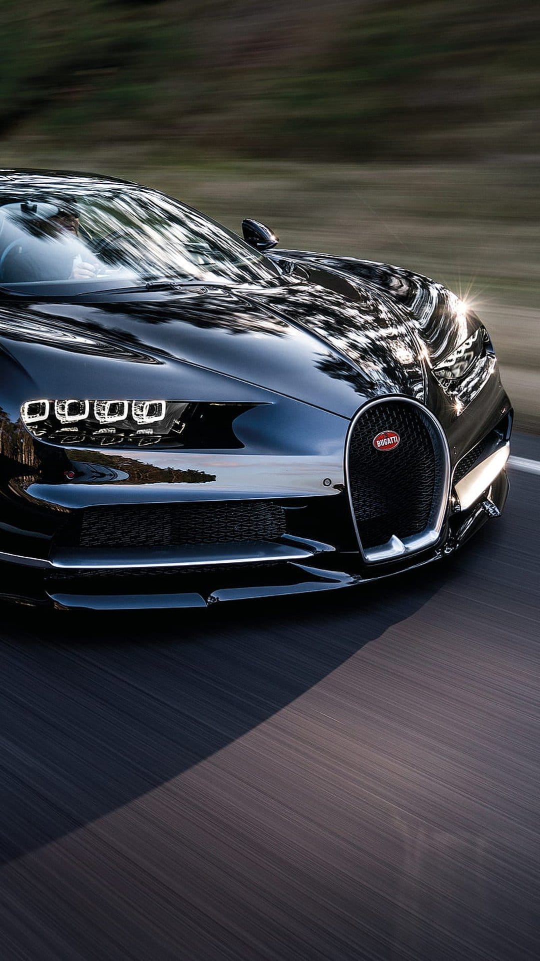 Bugatti Chiron hypercar in black paint speeding on a scenic highway with motion blur and bright headlights.