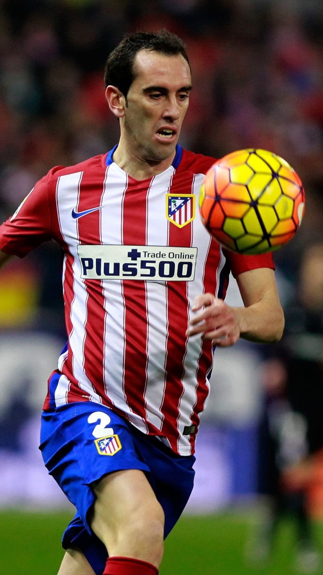 Diego Godín in a red and white striped jersey maneuvers a soccer ball across a green field during a stadium match.