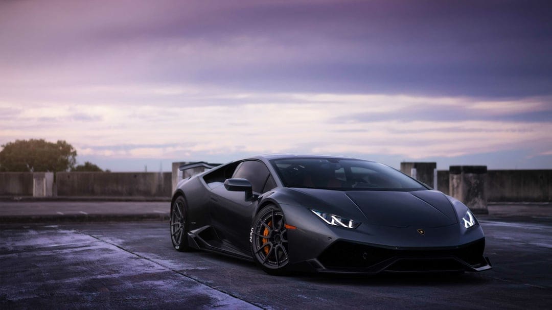 Dark grey Lamborghini Huracan with orange calipers on a rooftop under a purple twilight sky at dusk.