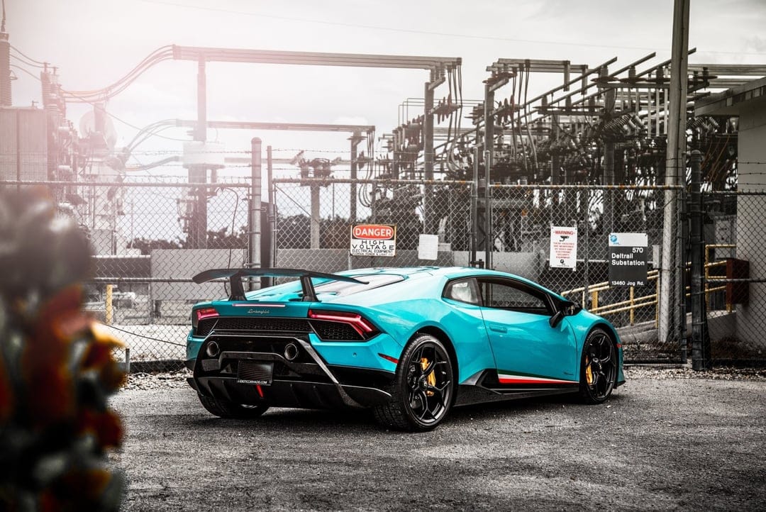 Cyan Lamborghini Huracan Performante parked at an electrical substation with industrial power lines and equipment.
