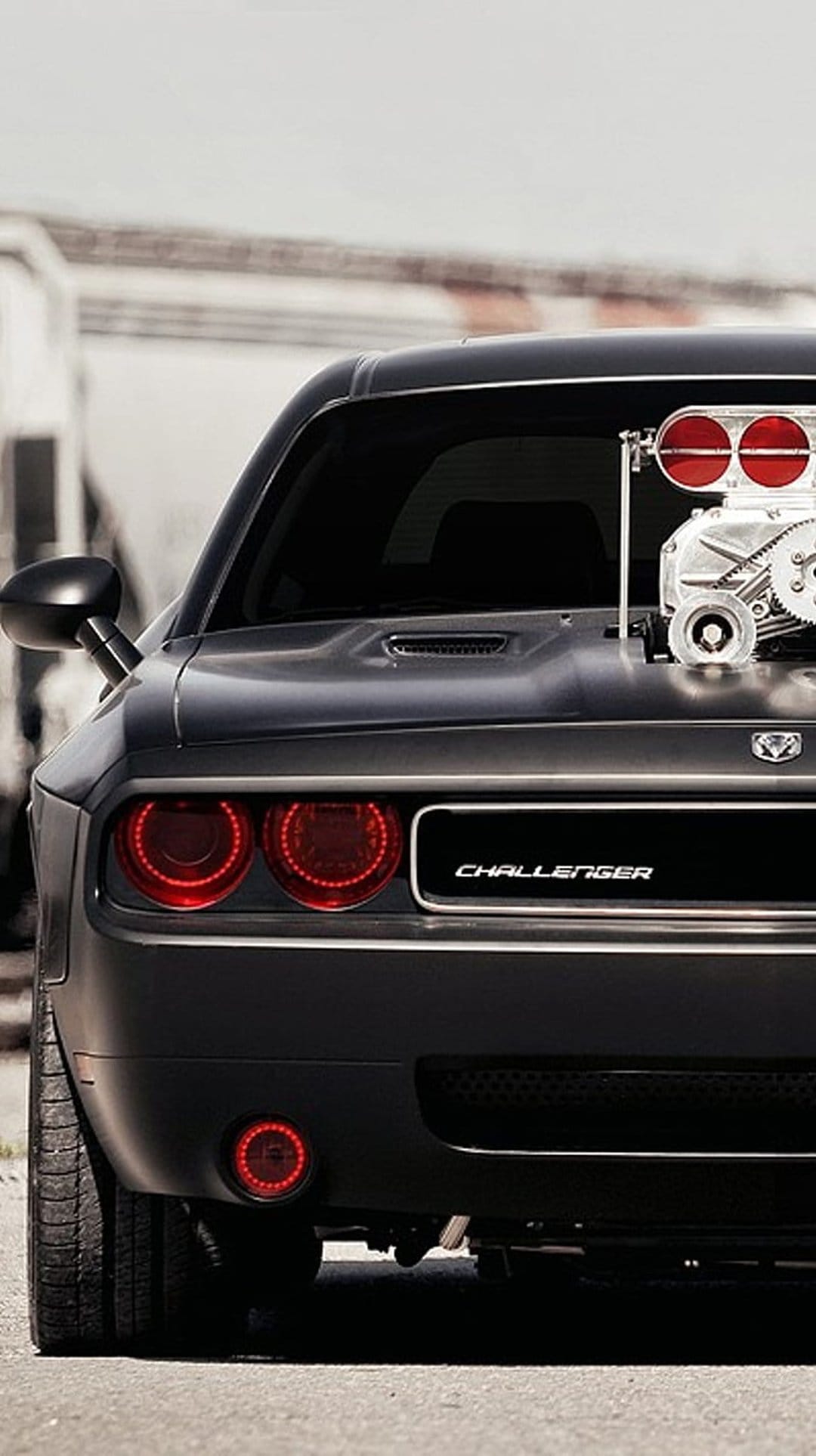 Matte black Dodge Challenger rear view features a chrome supercharger with red air intakes and round taillights.