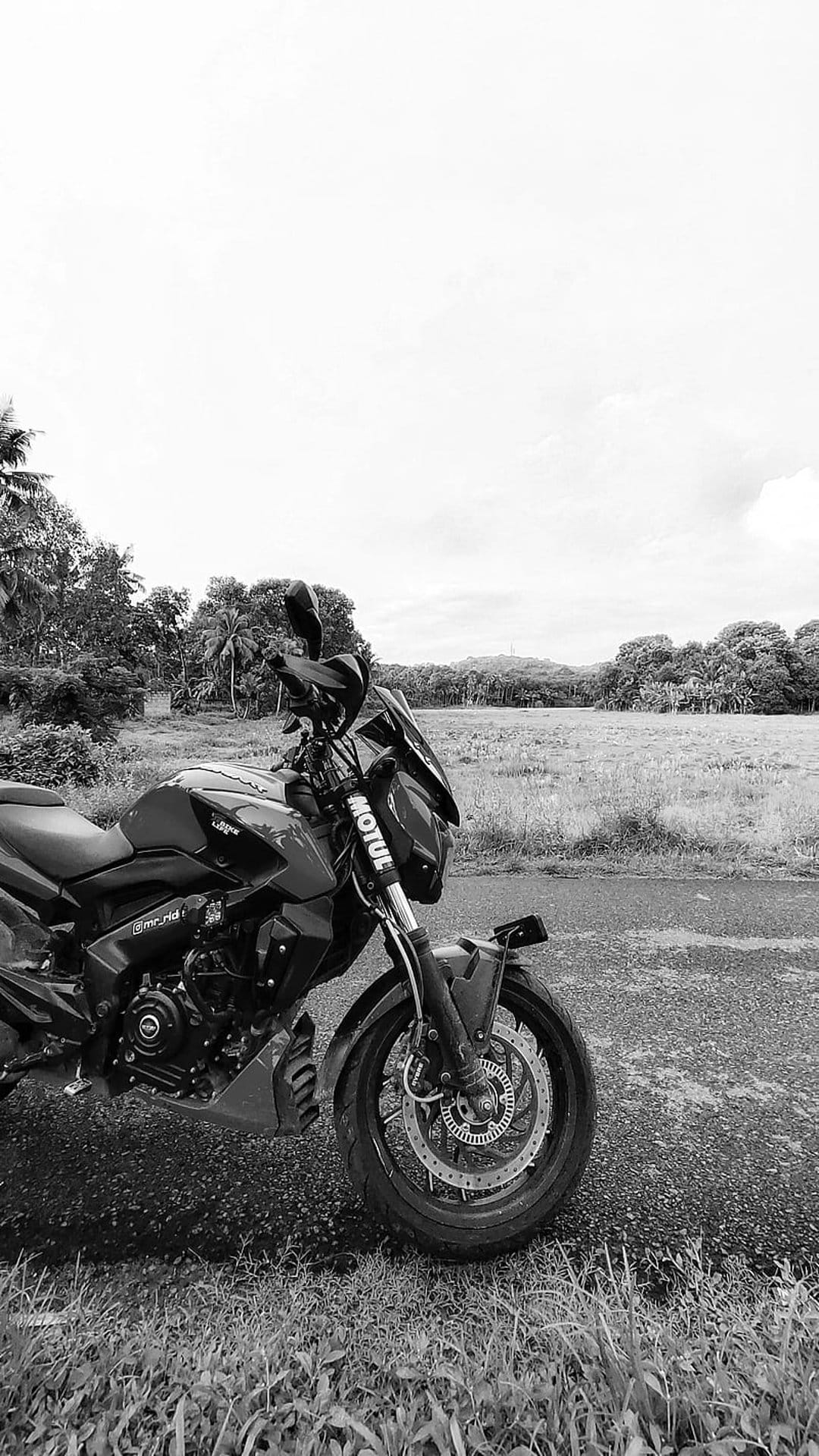 Black and white motorcycle parked on a country road with a vast grassy field and dark cloudy sky behind it.