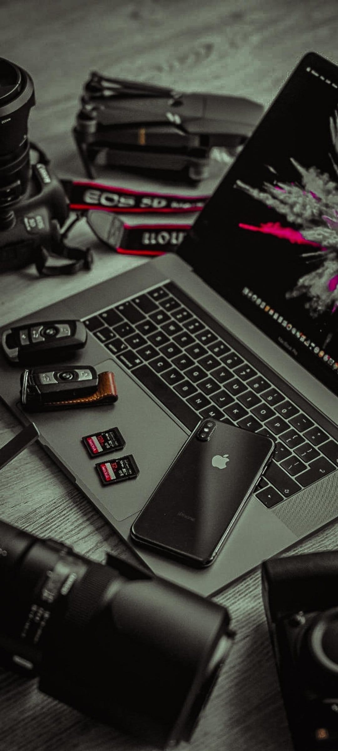 Photographer gear including a laptop, DSLR, drone, and phone on a wood surface in a flat lay composition.