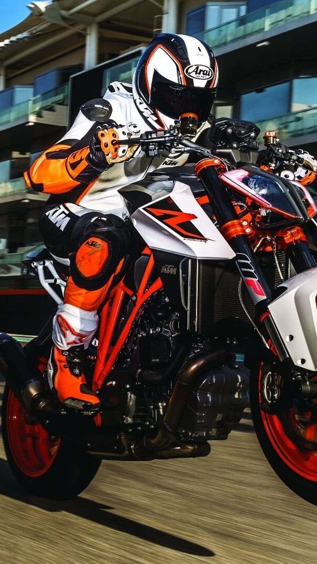 Motorcyclist in an orange racing suit leans a KTM sportbike into a sharp turn on a paved professional track.
