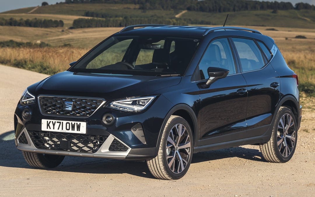 Dark blue SEAT Arona SUV parked on a gravel road with rolling hills under bright afternoon sunlight.