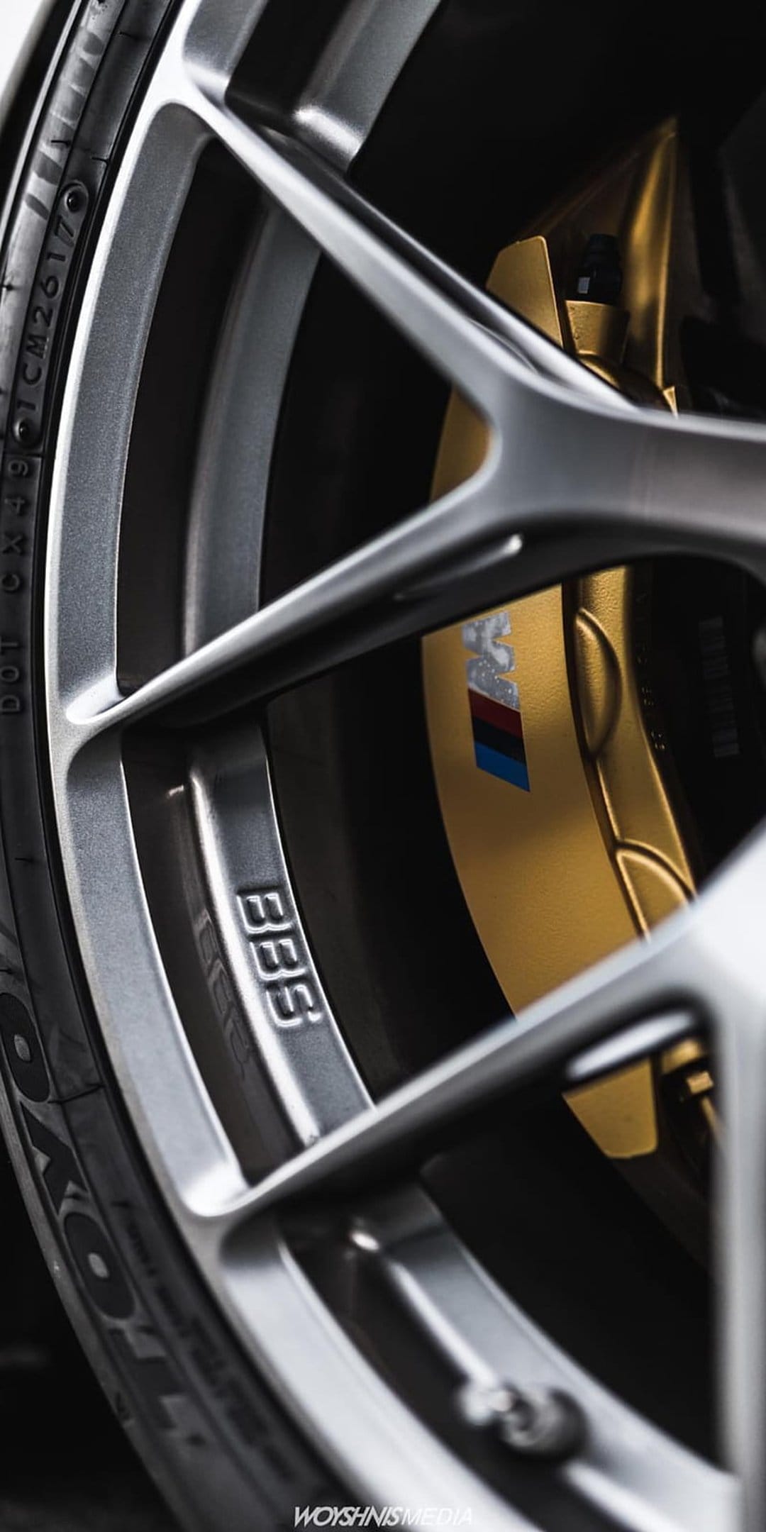 Gold M Sport brake caliper and silver BBS rim with a tri-color emblem shown in a detailed macro composition.