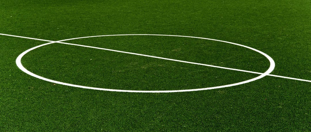 Green artificial soccer turf with a bright white center circle and straight line marking across the field.