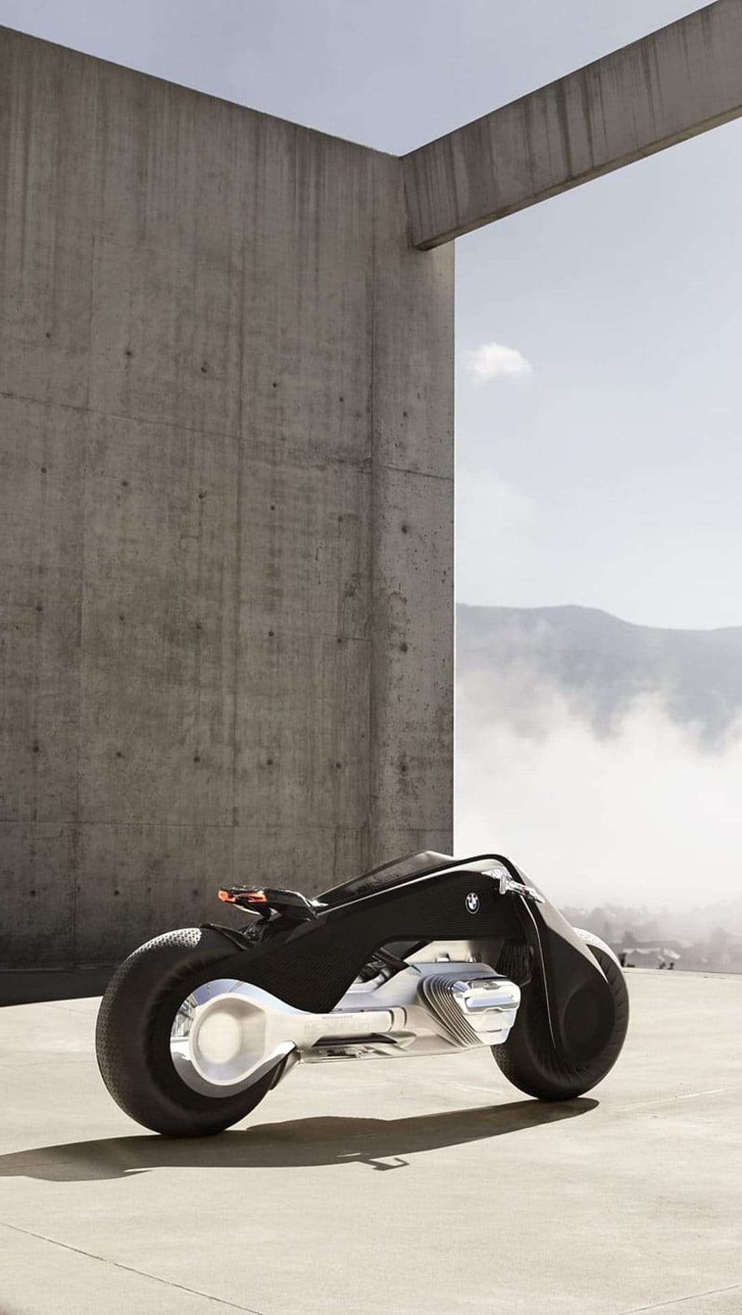 BMW Motorrad Vision Next 100 motorcycle on a concrete platform with misty mountains in the background.