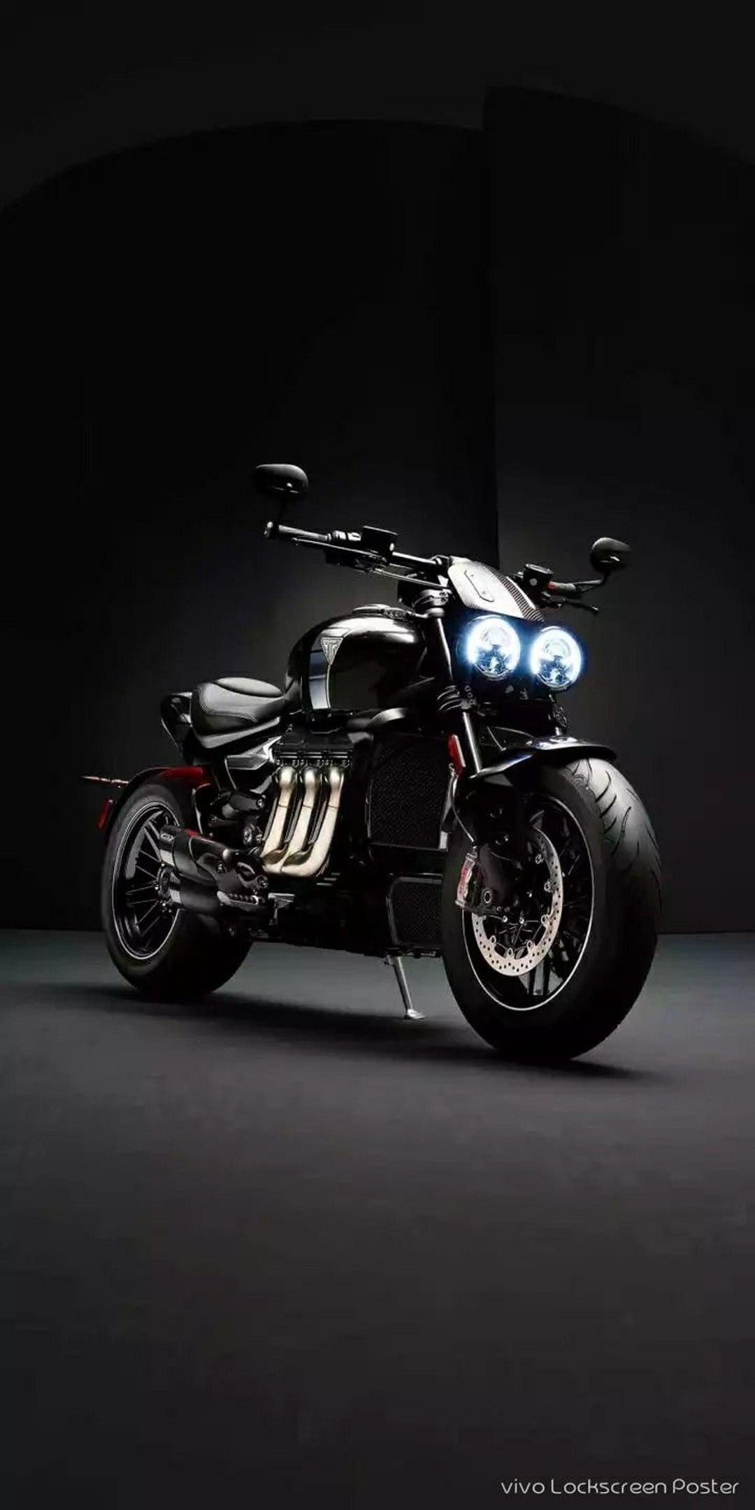 Triumph Rocket 3 motorcycle with dual circular LED headlights and chrome exhaust pipes against a dark backdrop.