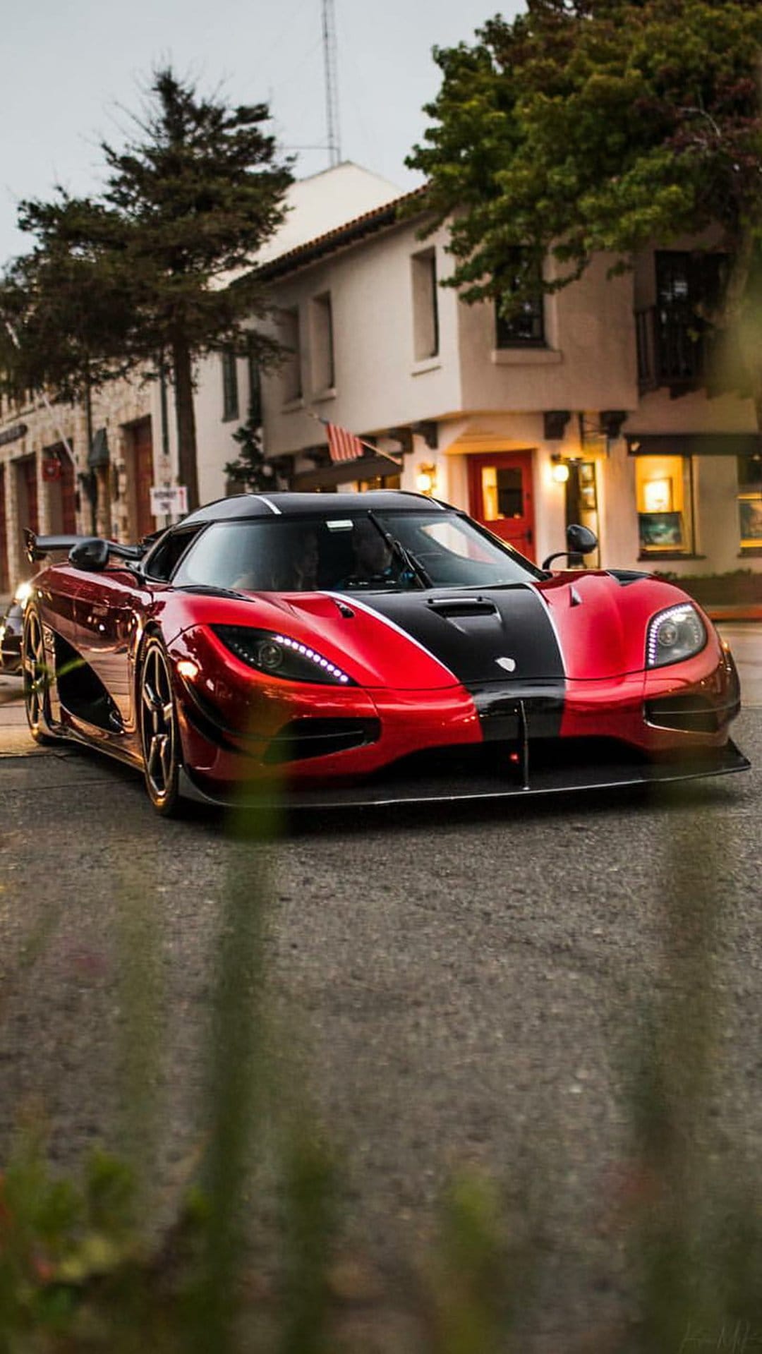 Koenigsegg Agera RS in red and black drives through a city at night with its bright LED headlights illuminated.