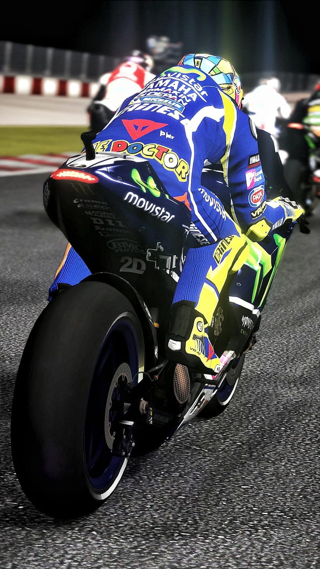 Motorcycle racer in a blue and yellow suit leans into a turn on a track with blurred bikes in the background.