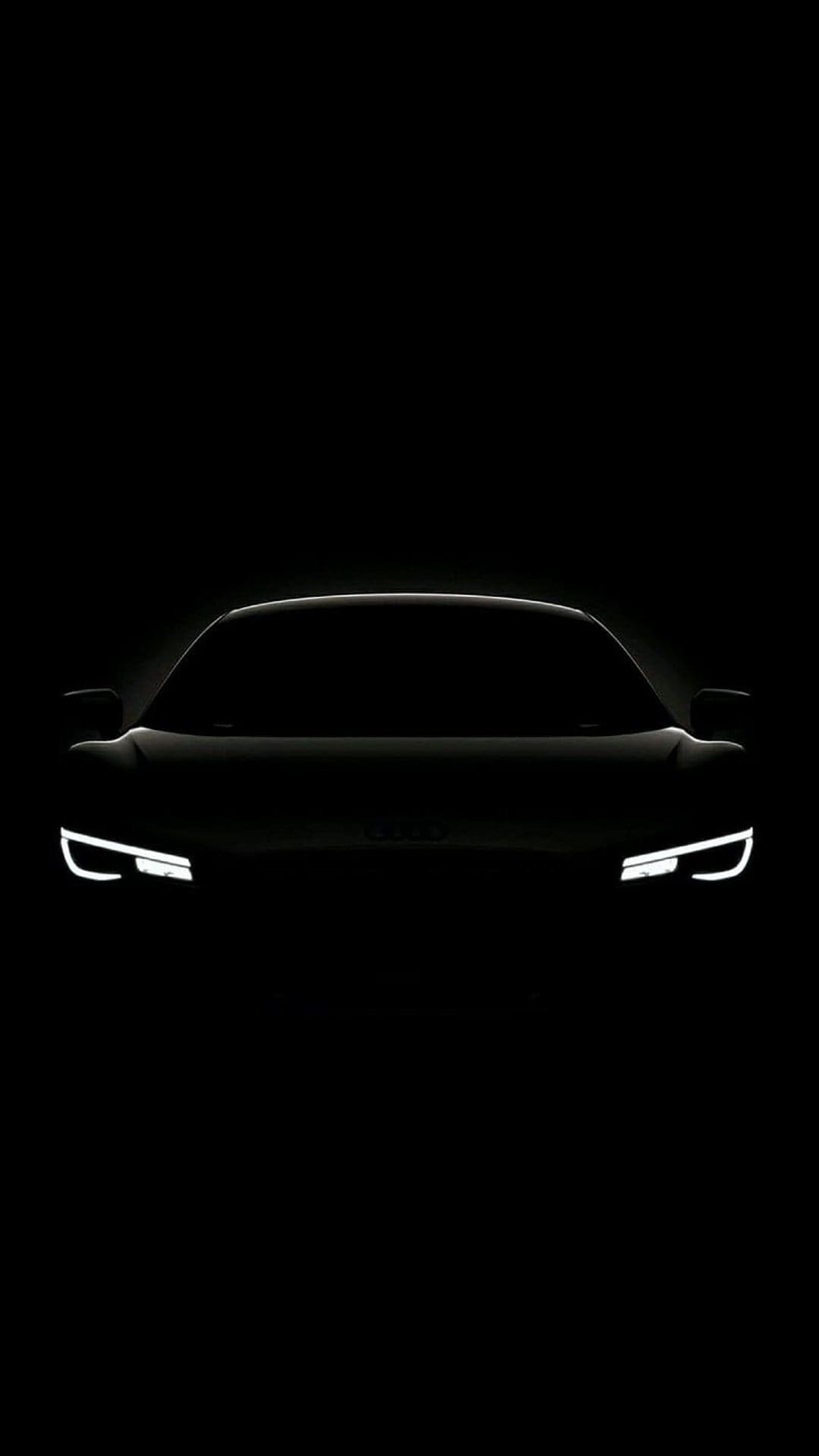 Sports car silhouette with glowing white LED headlights isolated against a solid pitch-black background.