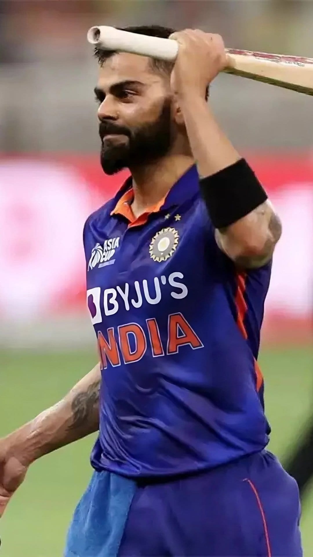 Virat Kohli raises his cricket bat while wearing a blue India jersey during a triumphant stadium celebration.