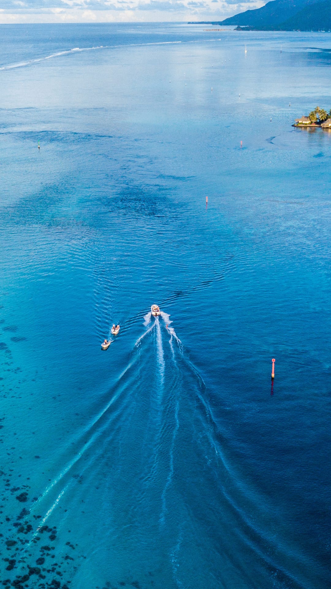 A small boat pulls two tubers across a vast turquoise ocean, leaving long white wakes on the calm water surface.