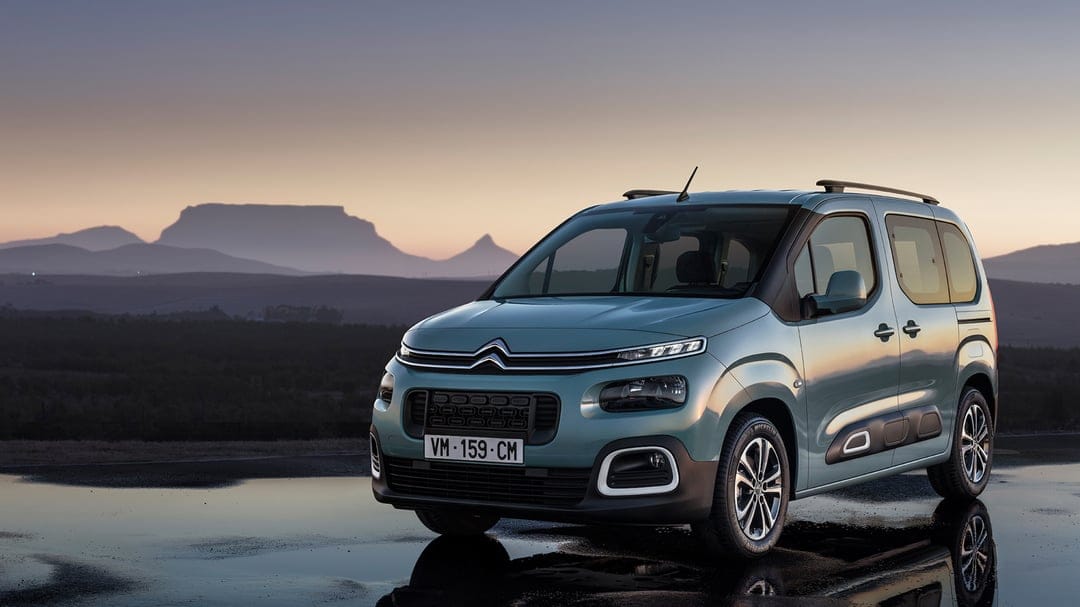 Teal Citroën Berlingo parked on a wet road with mountain silhouettes under a twilight sky background.