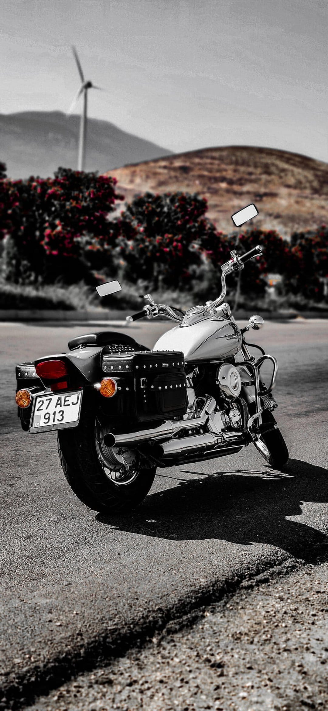 White cruiser motorcycle with chrome accents parked on asphalt with a wind turbine and red hills behind it.