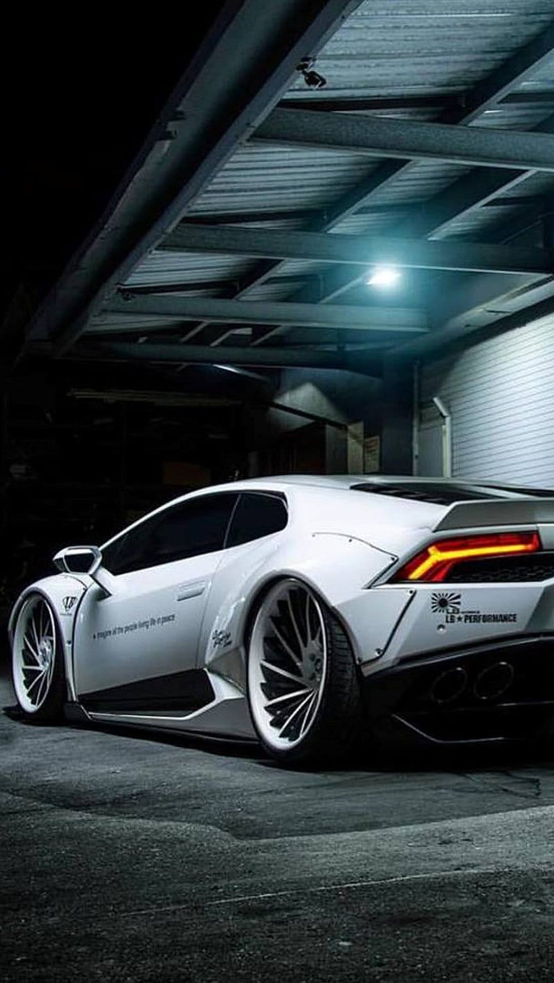 White widebody Lamborghini Huracan with aggressive fenders parked in a dark garage with dramatic lighting.