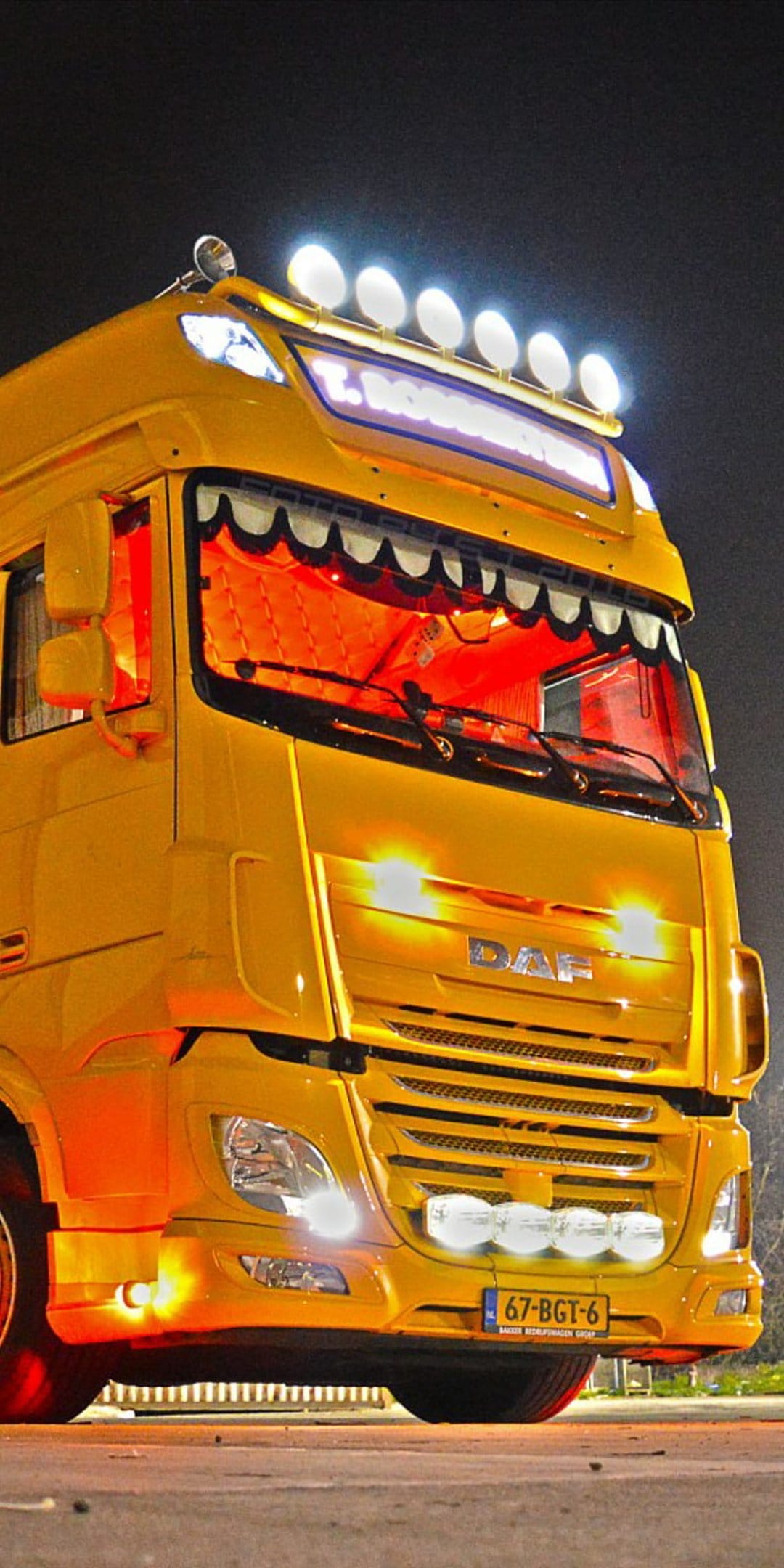Yellow DAF truck with bright white roof spotlights and a glowing orange interior parked in a dark night setting.