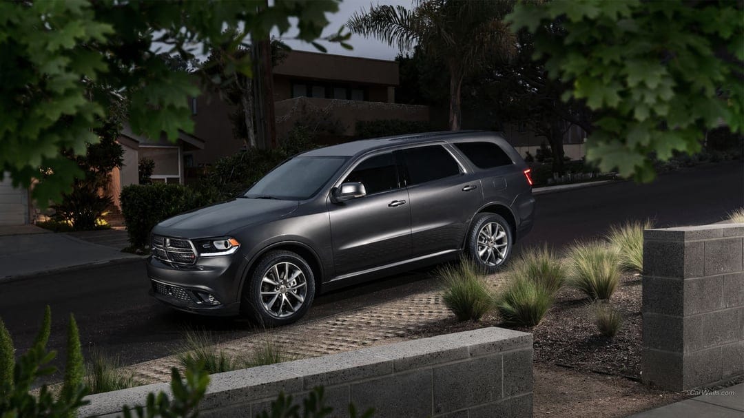 Charcoal Dodge Durango SUV parked on a paved driveway at dusk surrounded by suburban greenery and low walls.