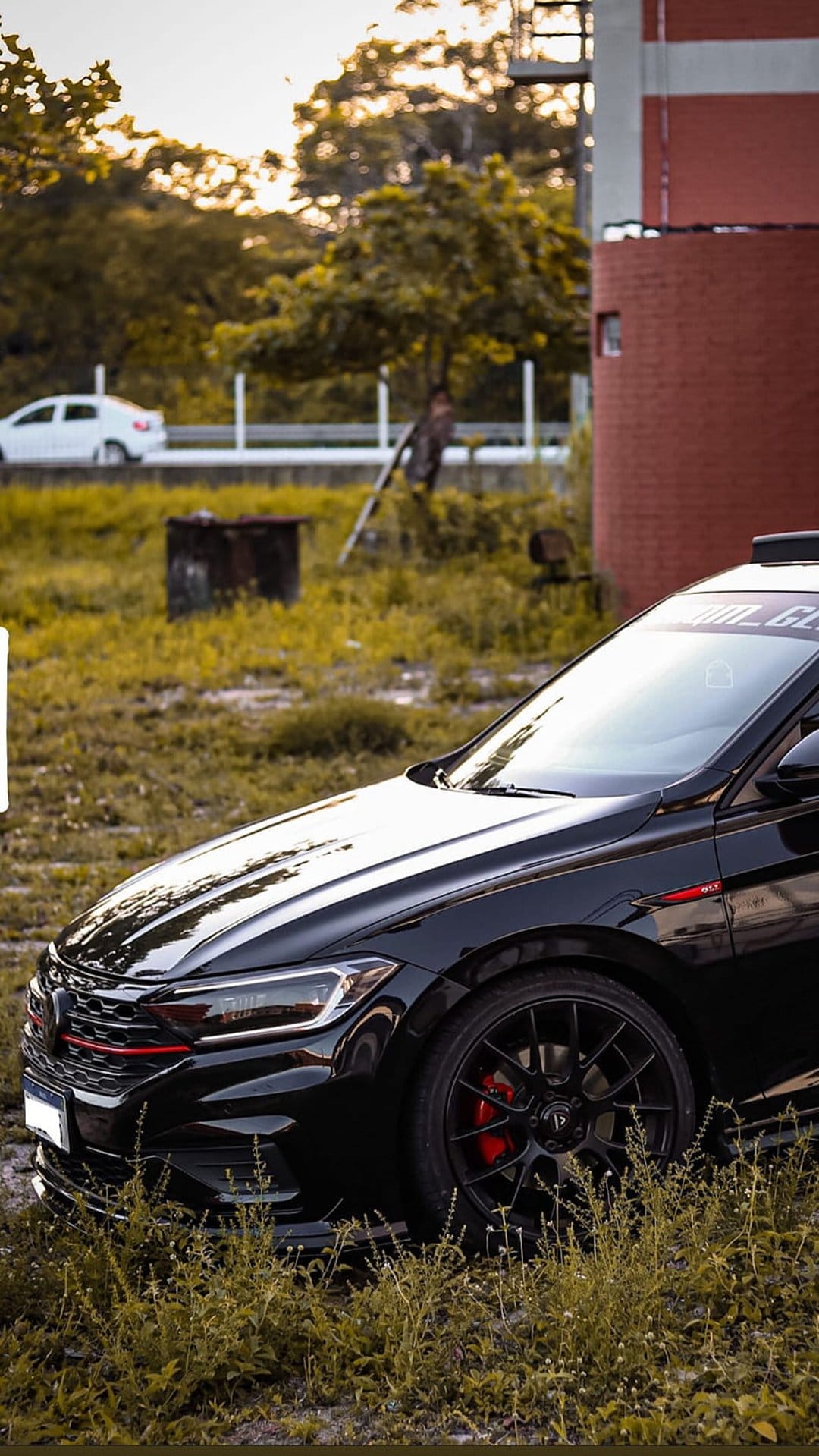 Black Volkswagen Jetta GLI sports car on a grassy field featuring red brake calipers and golden hour light.