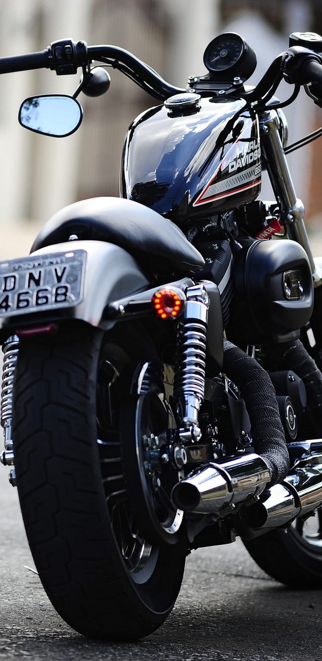 Black Harley-Davidson motorcycle rear showing chrome dual exhausts, a red tail light, and a metallic suspension.