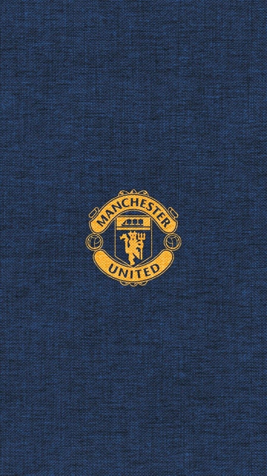 Manchester United crest in gold metallic finish centered on a dark blue textured fabric soccer jersey background.