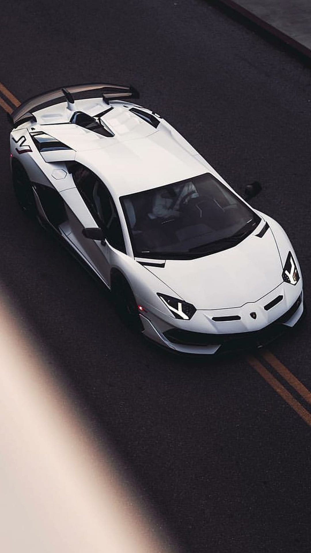 White Lamborghini Aventador SVJ parked on dark asphalt with yellow lane markings viewed from an overhead angle.