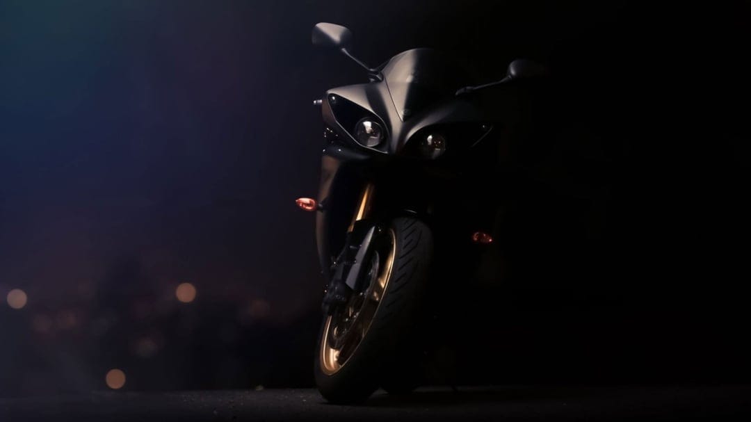 Black Yamaha R1 motorcycle with glowing headlights and gold rims in a dark, moody urban environment.