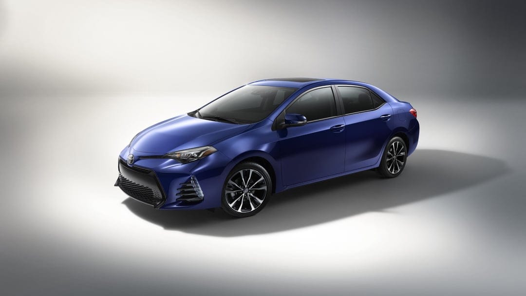 Deep blue Toyota Corolla sedan on a minimalist gray studio floor with soft overhead lighting and sleek alloy wheels.