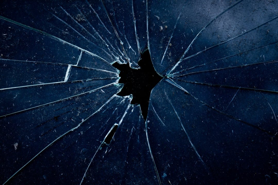 Fractured glass shards radiate from a central impact point with intricate midnight blue radial cracks.