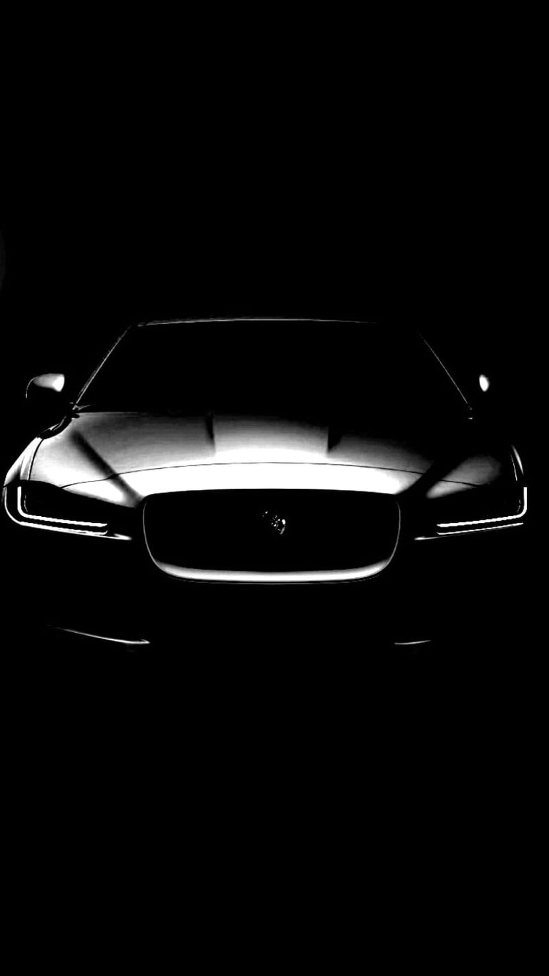Jaguar car headlights and mesh grille glow against a dark background with sharp, dramatic lighting effects.