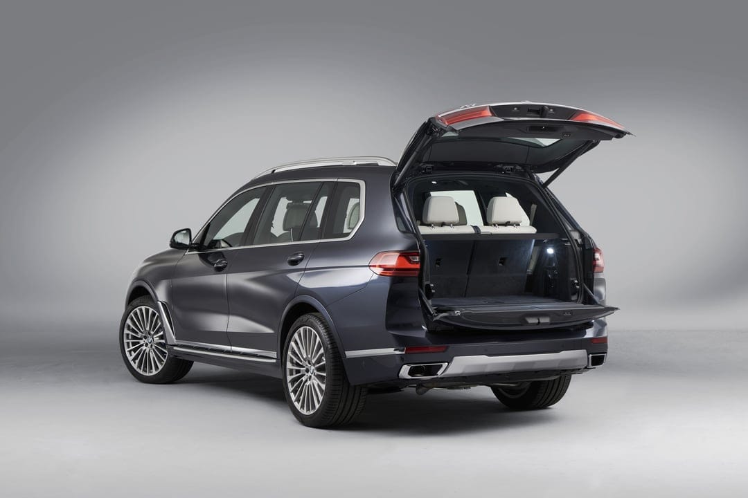 A dark blue luxury SUV with an open split tailgate showing white leather seats in a grey studio.