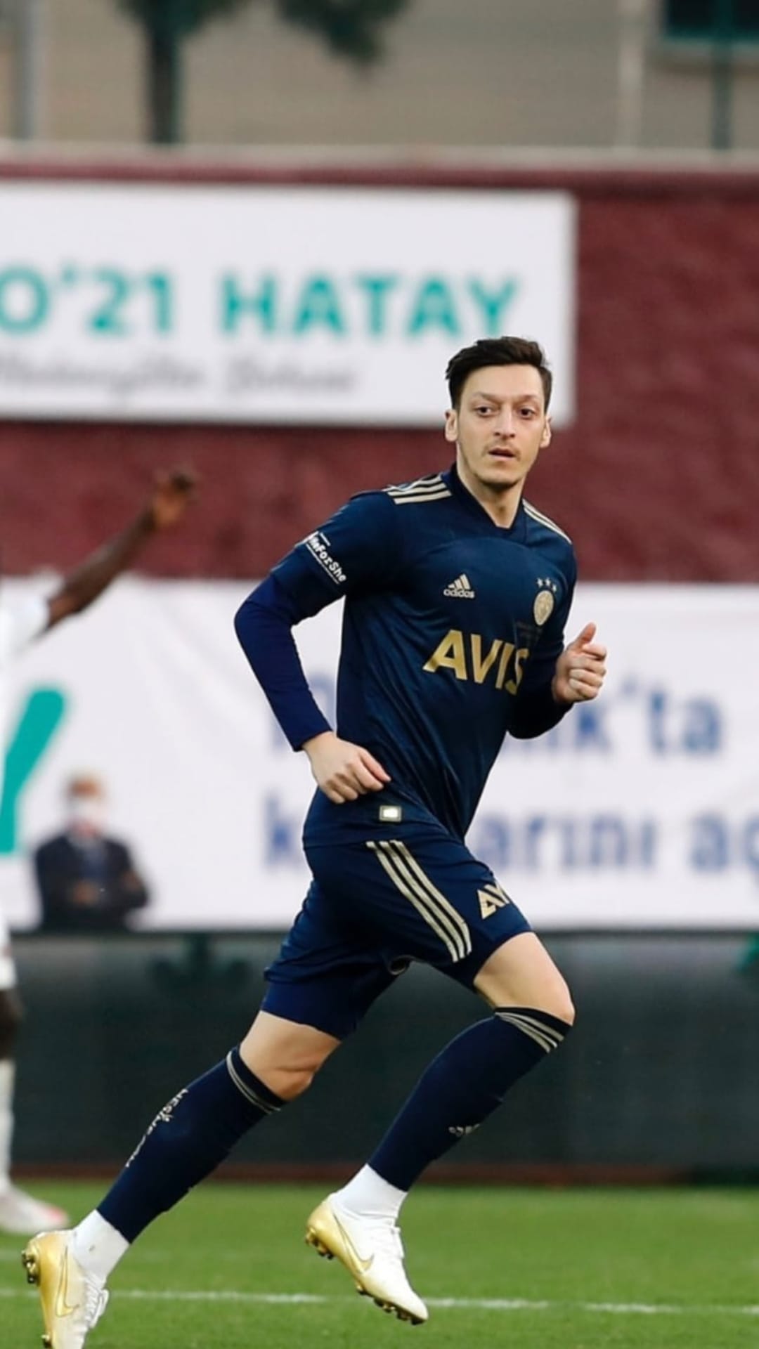 Mesut Ozil runs on a grass pitch wearing a dark blue Fenerbahce jersey with gold trim and metallic gold boots.