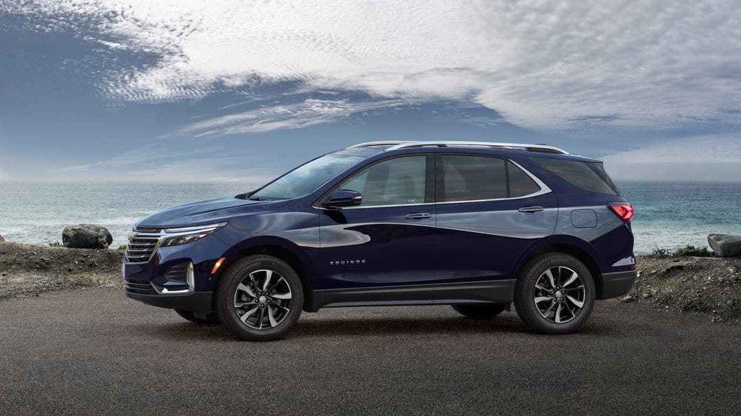 Dark blue Chevrolet Equinox SUV parked on a coastal road against a scenic ocean and cloudy sky background.