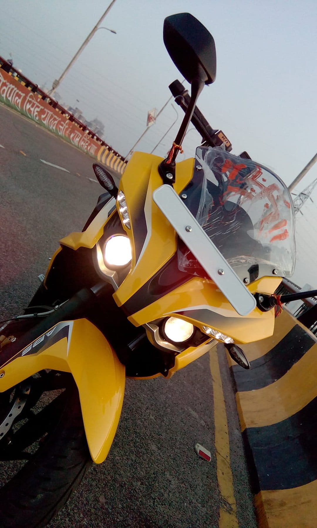 Yellow sportbike front fairing with bright headlights and red decals parked on an outdoor paved road.