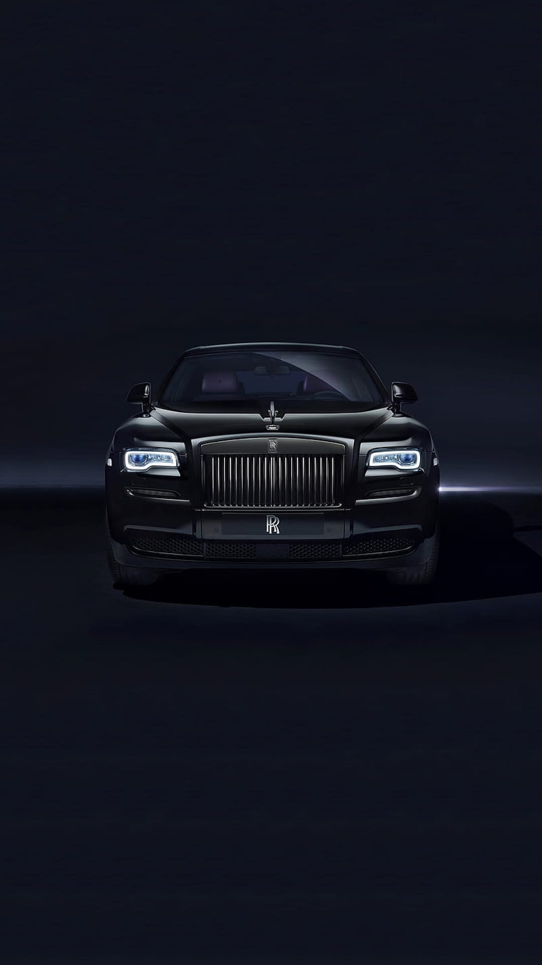 Rolls-Royce Ghost front grille and Spirit of Ecstasy ornament illuminated against a dark, minimalist background.