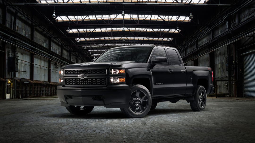 Black Chevrolet Silverado truck with amber lights glowing inside a dark, high-ceilinged industrial warehouse.