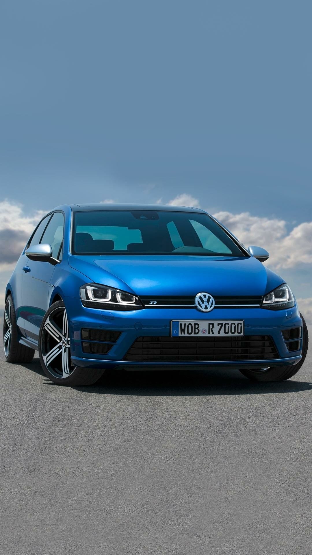 Blue Volkswagen Golf R hatchback parked on asphalt with LED headlights on under a bright blue sky with clouds.