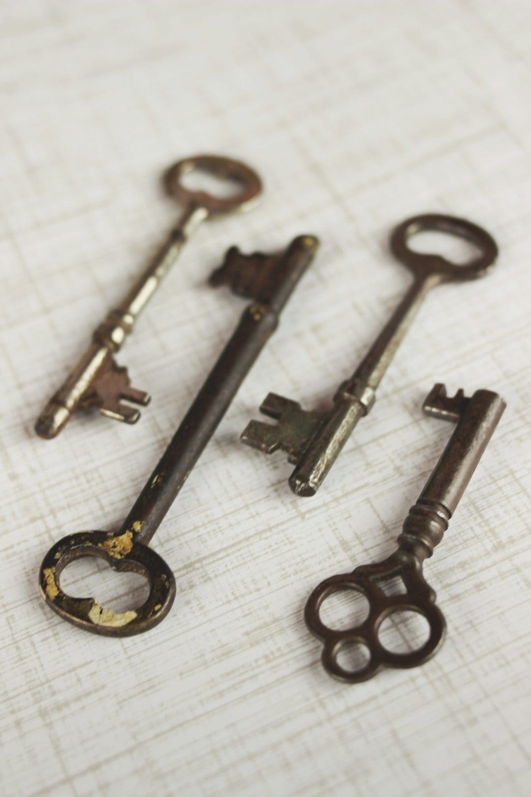 Four antique skeleton keys with rusted iron patinas are arranged on a white textured stone surface with shadows.