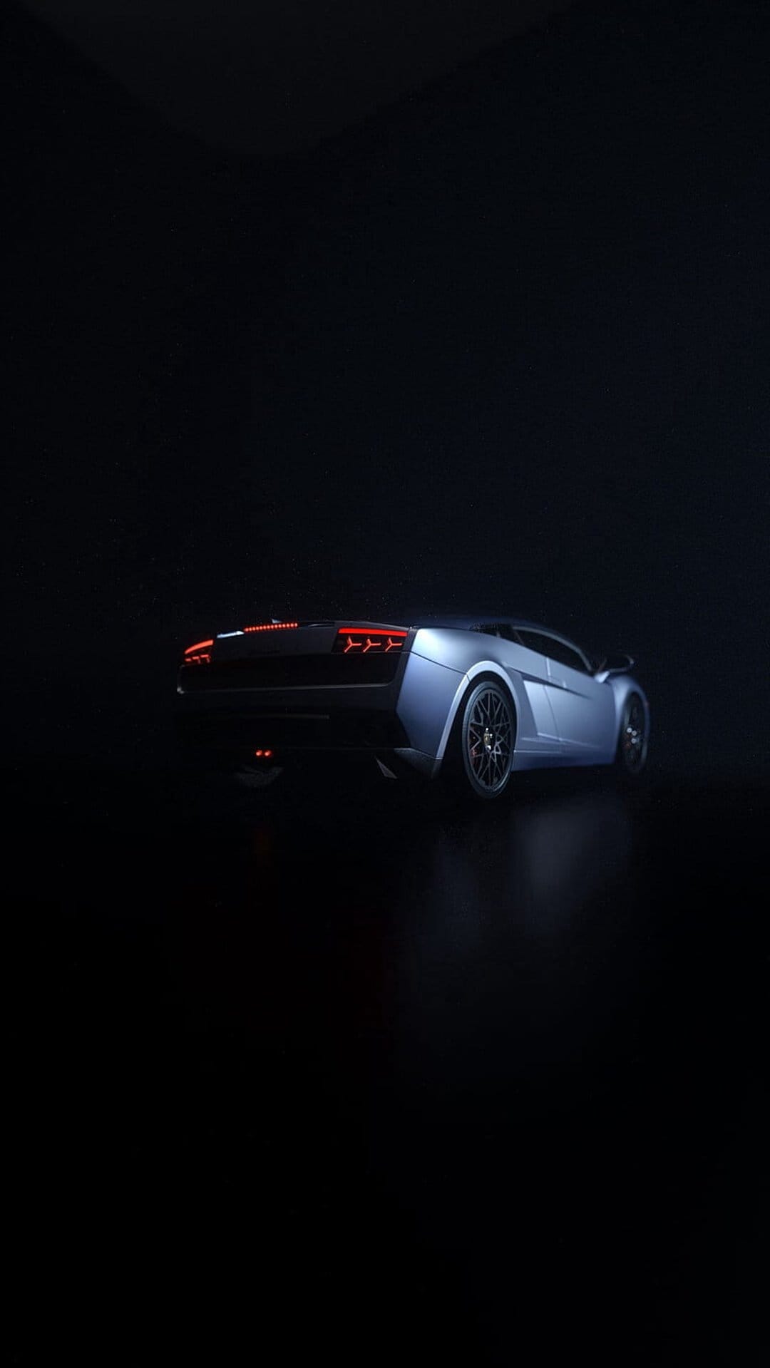 Silver sports car with glowing red taillights and metallic rims parked in a dark, low-key lighting environment.