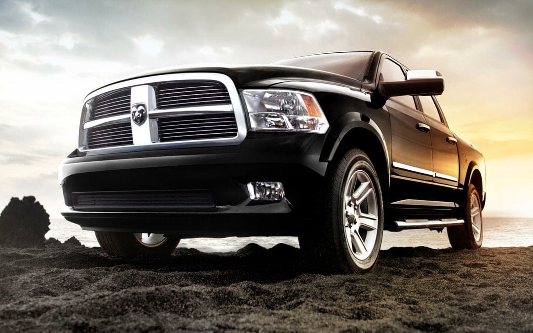 Black pickup truck with a chrome grille parked on a dark sandy beach under a dramatic golden hour sky.