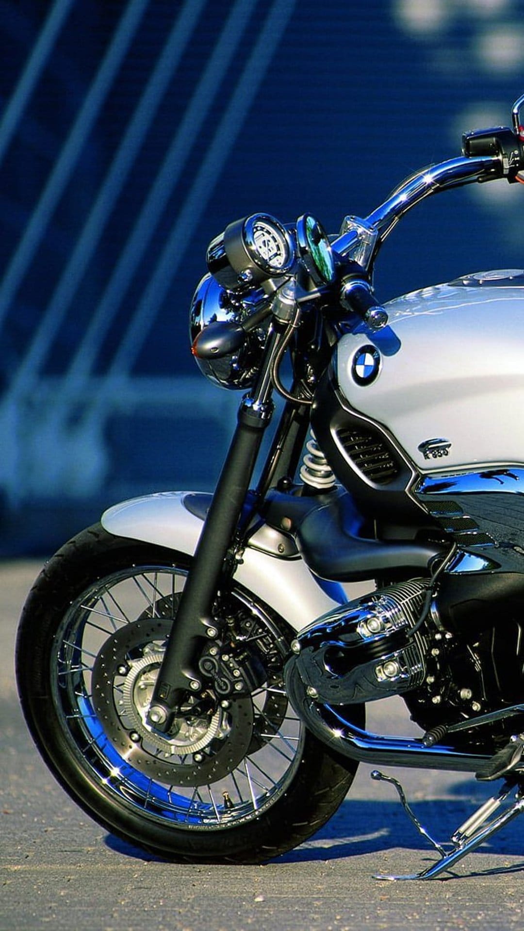 Silver BMW motorcycle front wheel and chrome engine components against a blue background with diagonal lines.